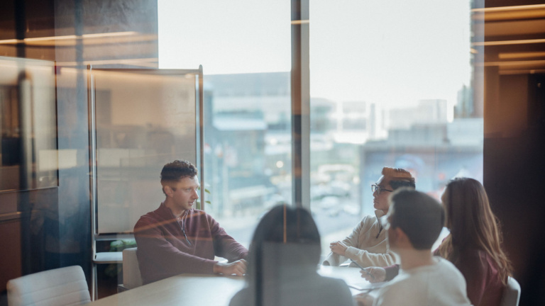 Photo of five people sitting around a table in a conference room